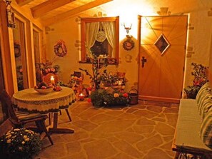 Una habitación acogedora con suelo de piedra, una mesa redonda con mantel de encaje, una silla de mimbre y una puerta de madera.