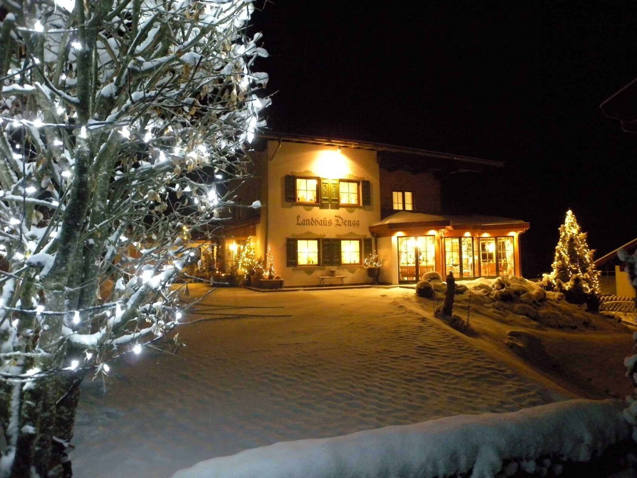 A building with a sign 'Landhaus Denga' at night, surrounded by snow and Christmas lights.