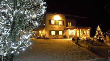 A building with a sign 'Landhaus Denga' at night, surrounded by snow and Christmas lights.