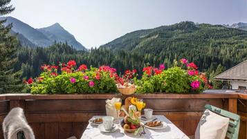 A table set with breakfast items, a wooden bench, and a view of mountains and forest.