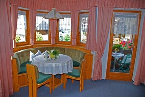A cozy room with a round table, green upholstered seating, and large windows with pink curtains. - Vacation apartment Bergpanorama for 2 to 4 persons - Landhaus Dengg (Gerlos)