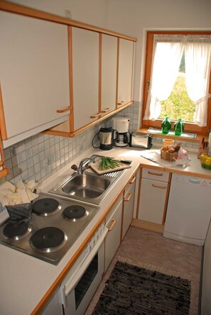 A compact kitchen with a sink, stove, and a window with curtains. - Vacation apartment Bergpanorama for 2 to 4 persons - Landhaus Dengg (Gerlos)