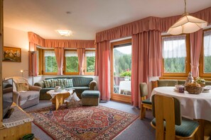 A cozy living room with a sofa, a table with a basket, and a view of greenery through large windows. - Vacation apartment Bergpanorama for 2 to 4 persons - Landhaus Dengg (Gerlos)