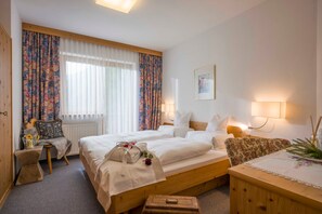 Ein Hotelzimmer mit zwei Betten, einem Holzkopfende, einem kleinen Tisch mit Lampe, einem Heizkörper und einem Fenster mit Vorhängen.