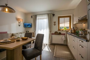 A modern kitchen with a dining area, a TV, and a window with curtains.
