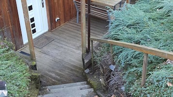 Eine Holztreppe führt zu einem überdachten Außenbereich mit einer Bank und einem Tisch.
