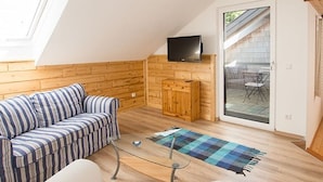 Un espacio tipo loft con piso de madera, un sofá a rayas, una mesa de centro de vidrio y un televisor en la pared.