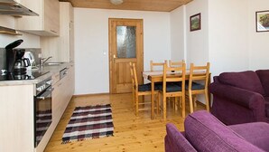 Un espacio habitable compacto con kitchenette, mesa de comedor de madera, sofá púrpura y alfombra escocesa.