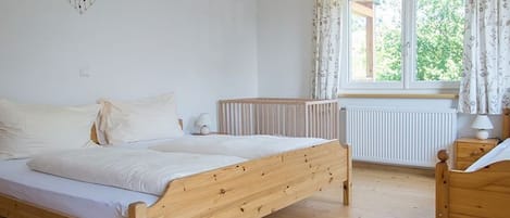 A bedroom with a wooden bed, a radiator, a window with curtains, and a heart-shaped decoration on the wall.