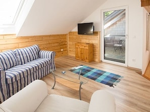 Un espacio tipo loft con piso de madera, un sofá a rayas, una mesa de centro de vidrio y un televisor en la pared.