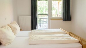 Una cama individual con estructura de madera, ropa de cama blanca y vistas a una terraza exterior a través de una ventana.