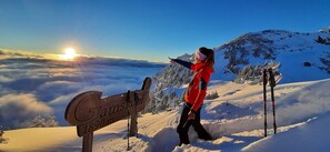 Ein hölzernes Wegweiser mit der Höhenangabe 'Tamsberg 1890 m', eine Person in roter und schwarzer Kleidung sowie Ski-Stöcke auf einem verschneiten Berghang.