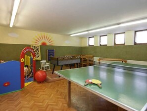 Ein Zimmer mit Tischtennisplatte, Kicker und einem Spielbereich mit Bällebad und Klettergerüst.