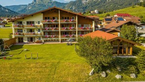 A multi-story hotel with balconies adorned with flowers, set against a mountainous backdrop. - No. 8 Bergaster - HAUS fern (Grän)
