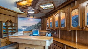 A wooden reception desk with a computer, a shelf with magazines, and a wall with framed pictures. - No. 8 Bergaster - HAUS fern (Grän)