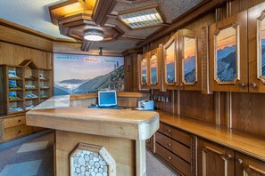 A wooden reception desk with a computer, a shelf with magazines, and a wall with framed pictures. - No. 8 Bergaster - HAUS fern (Grän)