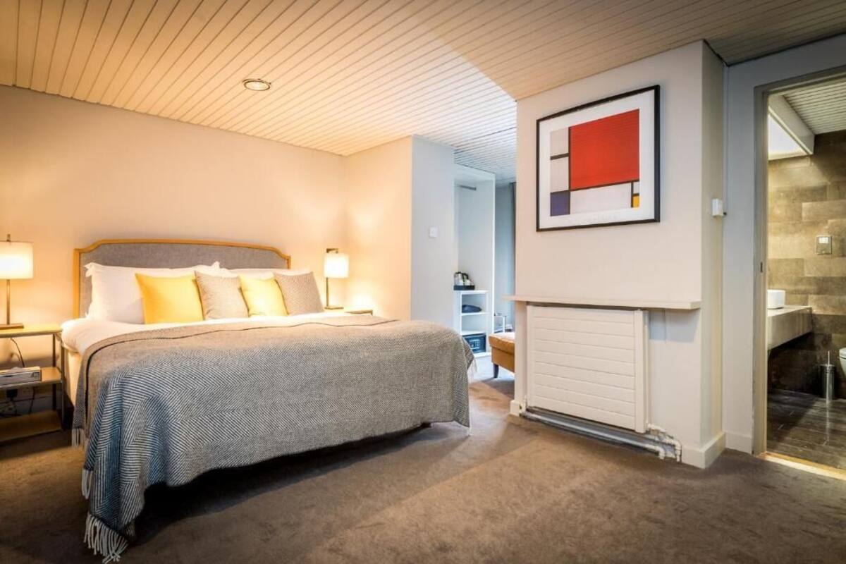 A bedroom with a bed, bedside lamps, a fireplace, and a framed artwork on the wall.