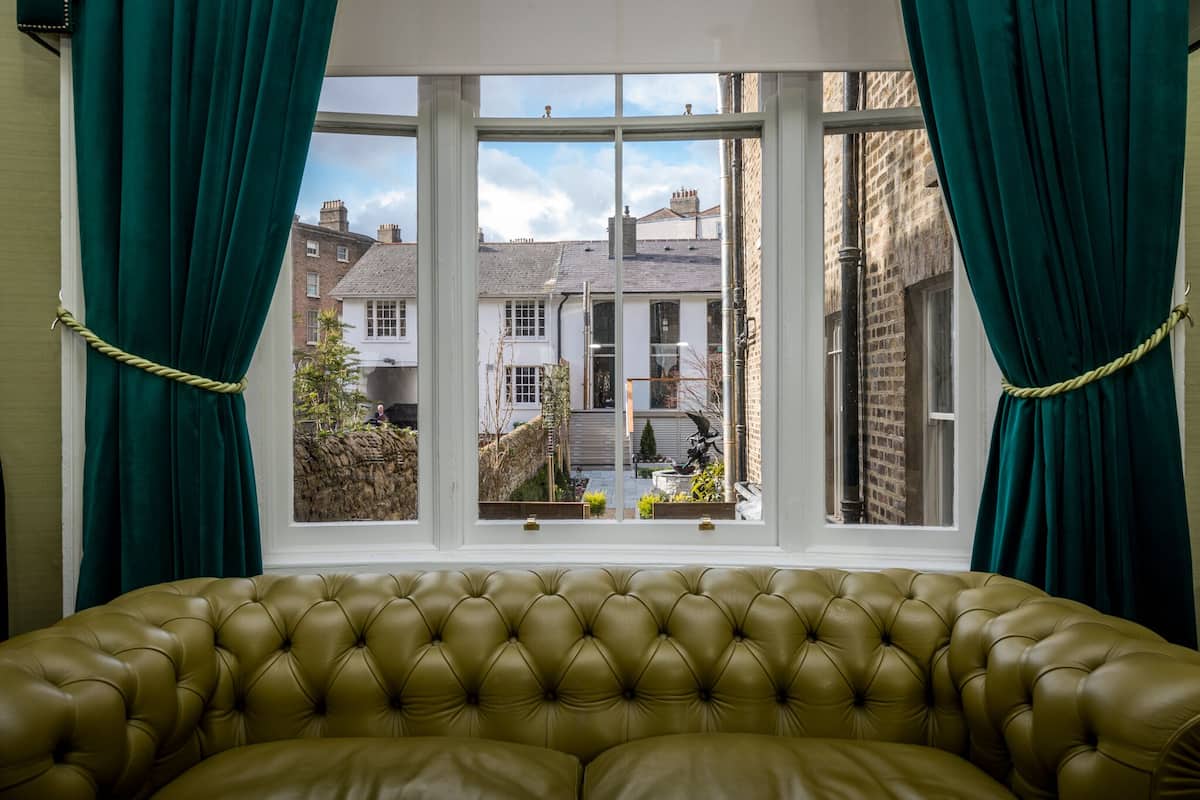 A room with a large window, green curtains, and a brown leather sofa.