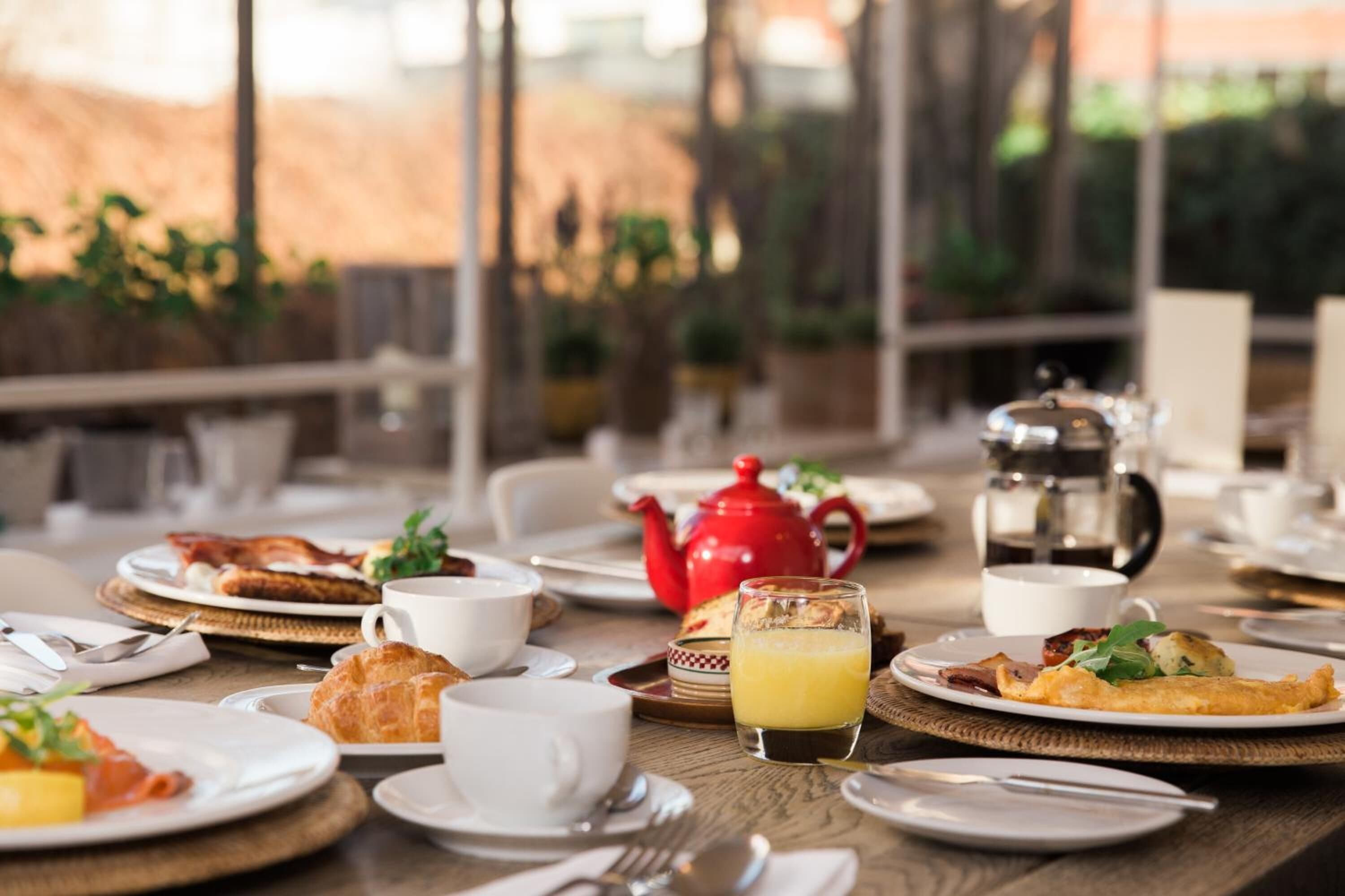 A breakfast setting with plates of food, cups, and a teapot on a table.
