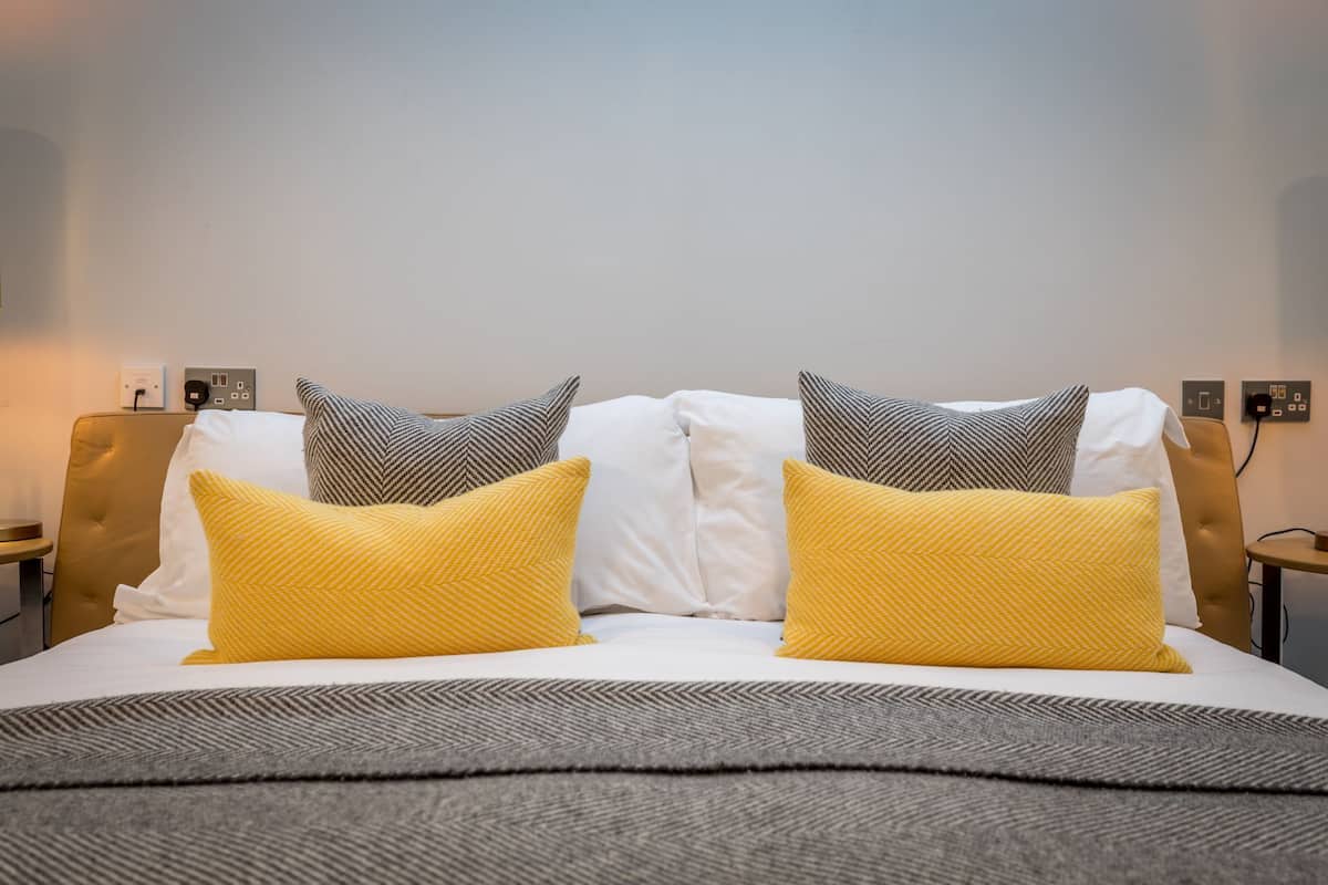 A neatly made bed with white and yellow pillows, a grey blanket, and a wooden headboard.