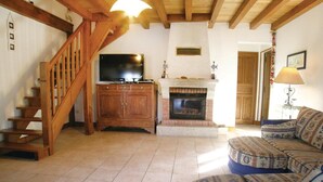 Una sala de estar con chimenea, una escalera de madera y un televisor sobre un mueble.