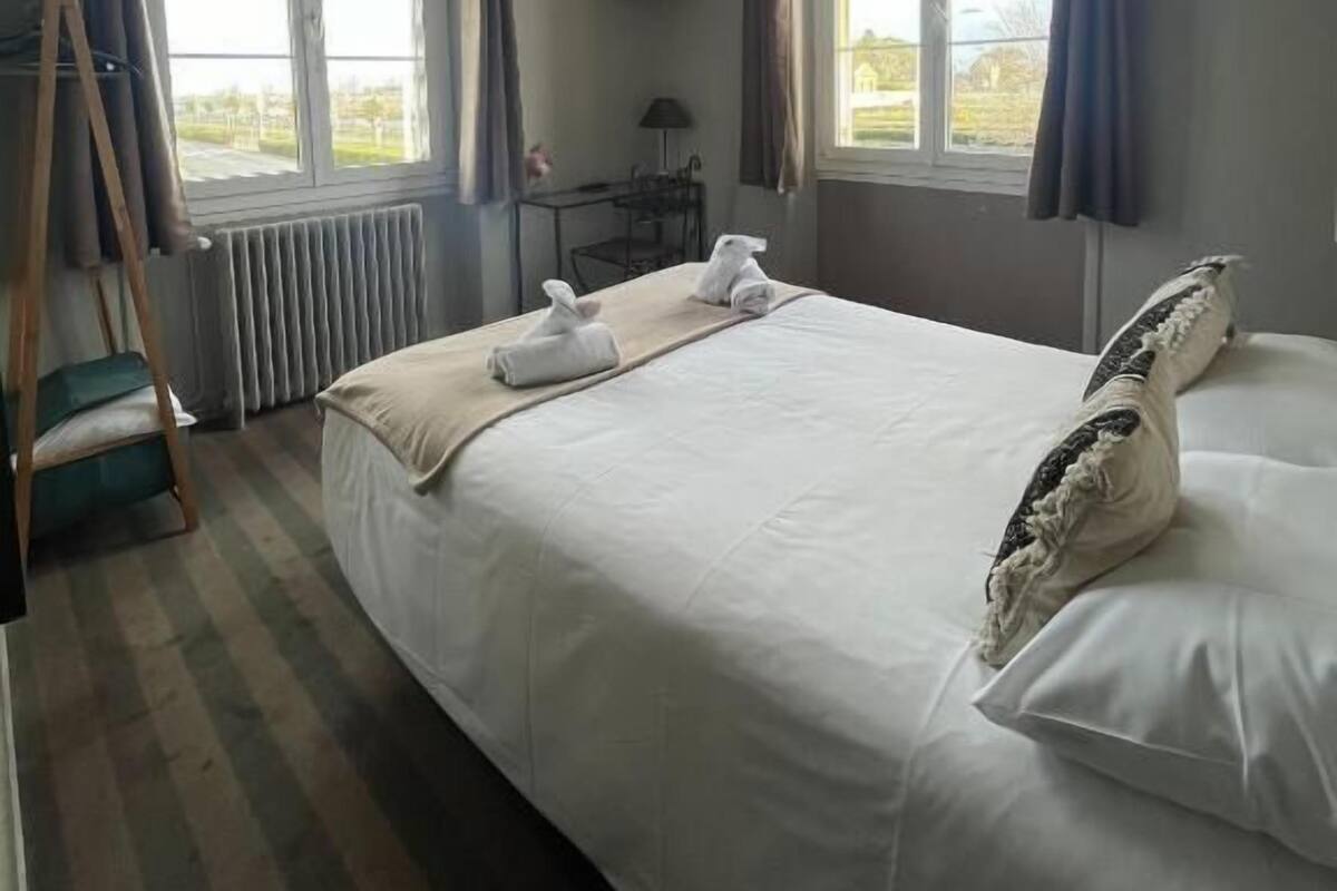 Habitación de hotel con una cama grande, dos ventanas, un televisor, un escritorio y una silla.