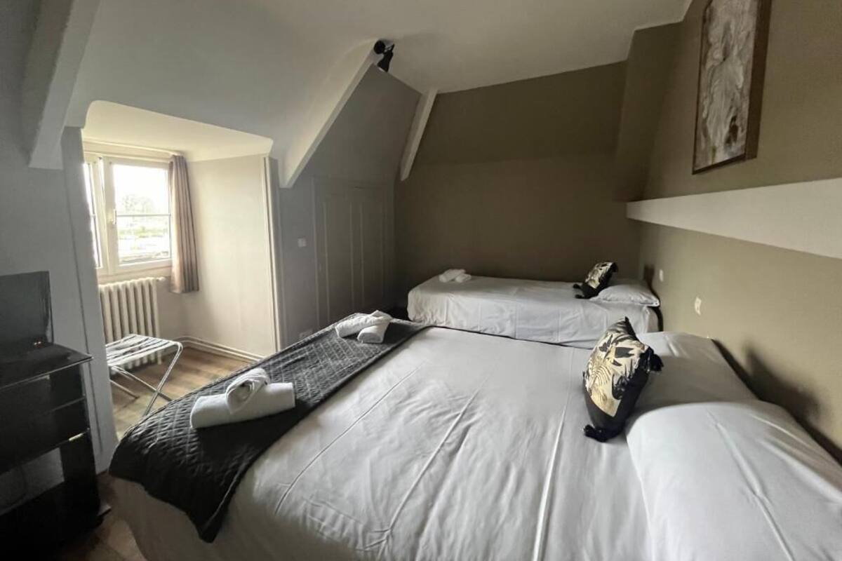 Habitación de hotel con dos camas, televisión, radiador y ventana con cortinas.