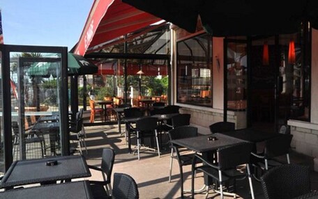 An outdoor cafe area with tables and chairs, a glass enclosure, and a red awning.