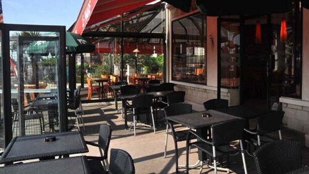 An outdoor cafe area with tables and chairs, a glass enclosure, and a red awning. - Hôtel du Phare (Ouistreham)