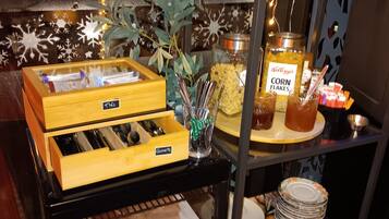 A buffet setup with various food items, including cereal, condiments, and utensils.