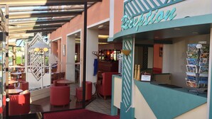 A reception area with a counter, a display of postcards, and red seating. - Hôtel du Phare (Ouistreham)