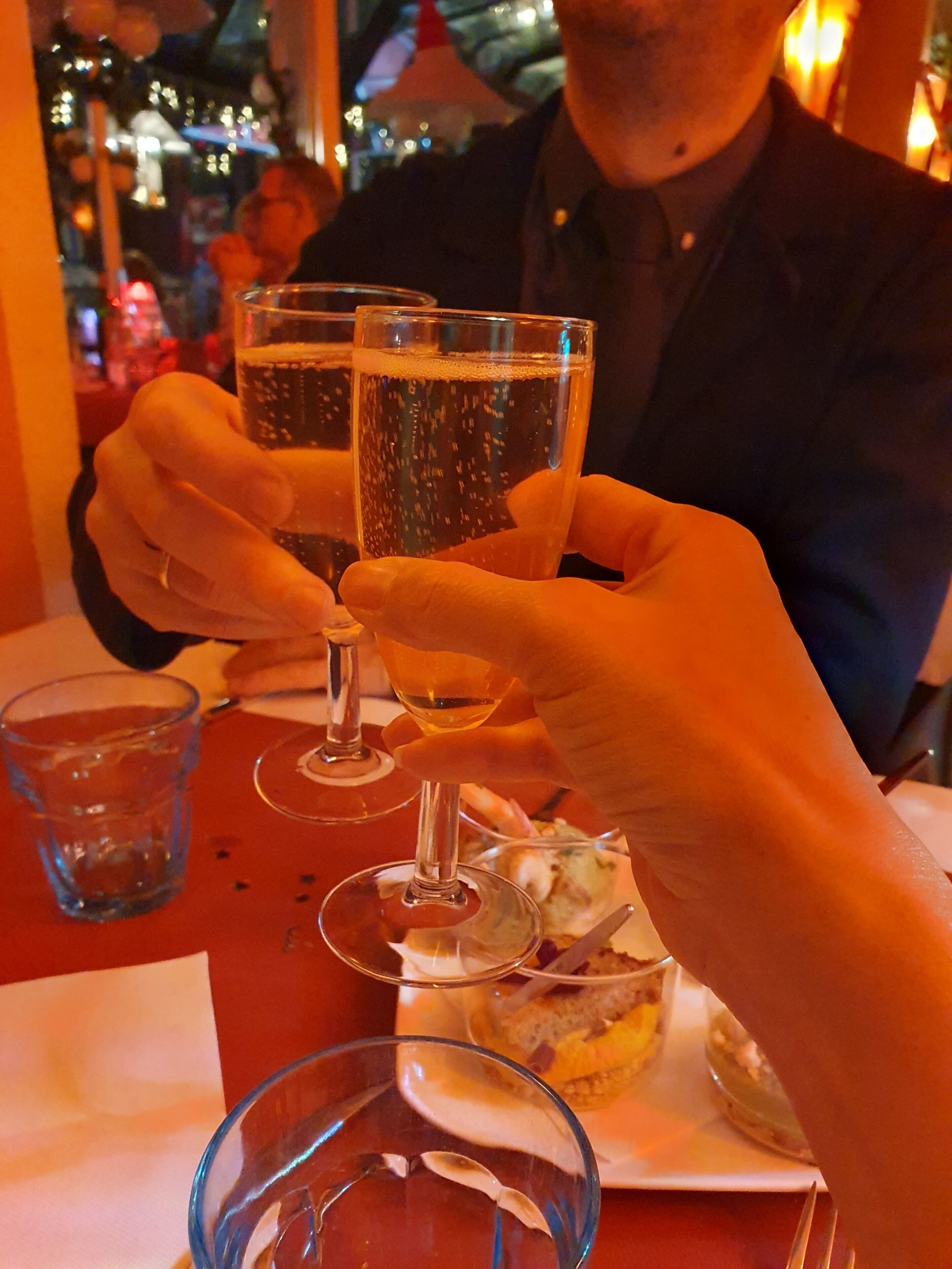 A person holding two glasses of a bubbly beverage at a table with a dessert plate.