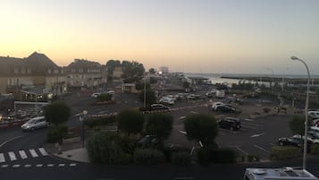 Un parking où sont garées plusieurs voitures et un fourgon, entouré d’immeubles et bordé par une route menant à un pont.