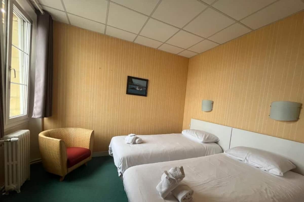 Una habitación de hotel con dos camas, una silla, un radiador y un cuadro en la pared.