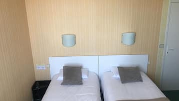 A hotel room with two beds, each with a headboard, a bedside table, and a wall-mounted lamp.