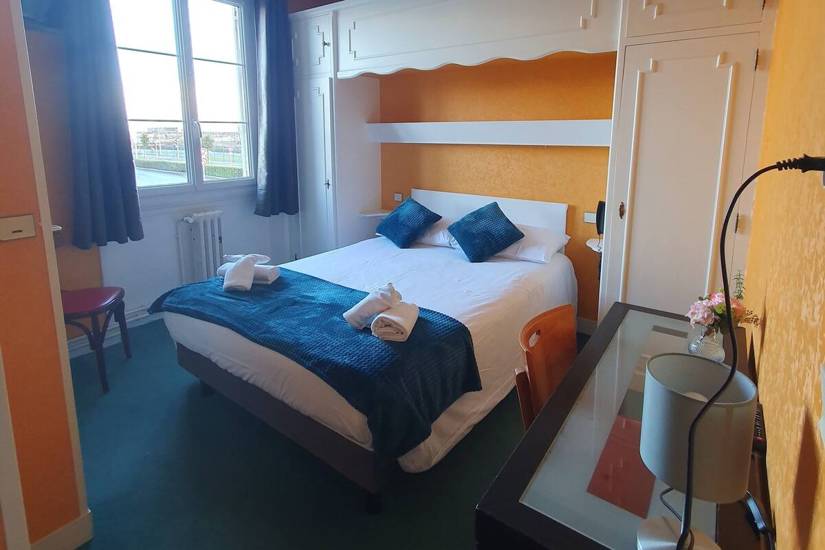 Habitación de hotel con cama, escritorio, silla, ventana y detector de incendios en el techo.