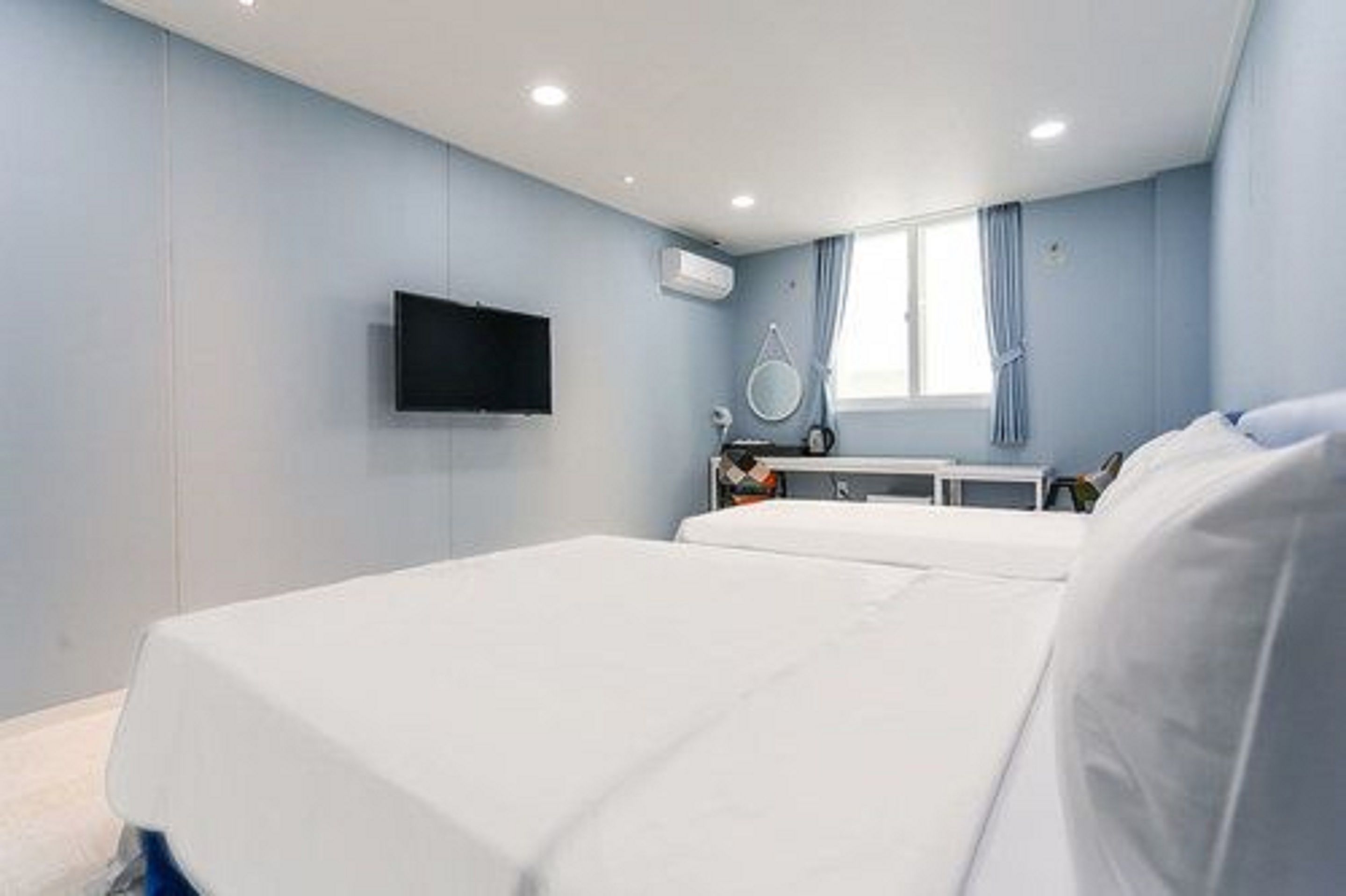 Ein Hotelzimmer mit zwei Betten, einem Flachbildfernseher, einer Klimaanlage, einem Nachttisch und einem Fenster mit Vorhängen.
