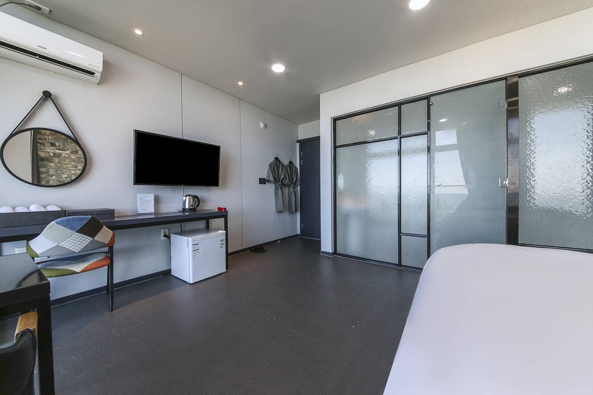 Une chambre d’hôtel moderne équipée d’une télévision à écran plat, d’un bureau avec un ordinateur, d’un petit réfrigérateur, d’une grande fenêtre offrant une vue agréable et d’un lit.