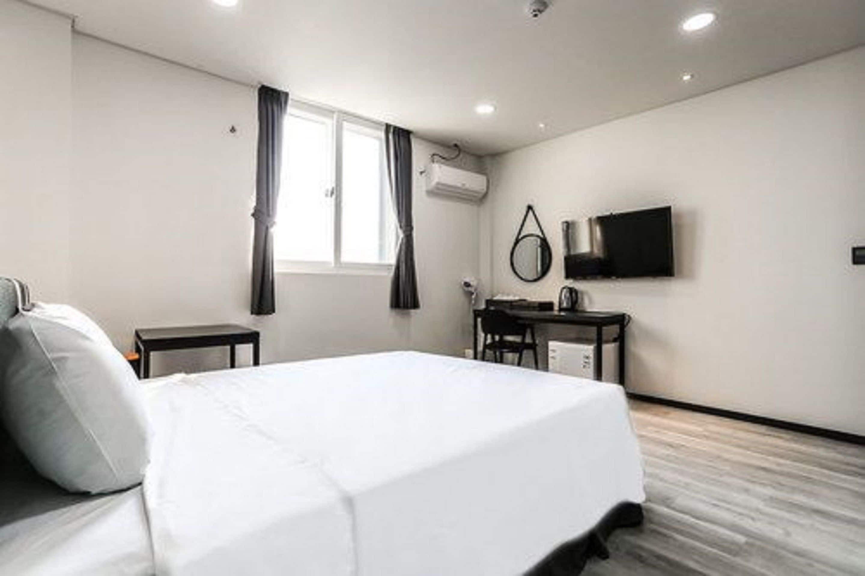 A hotel room with a bed, a desk, a chair, a TV, and a window with curtains.