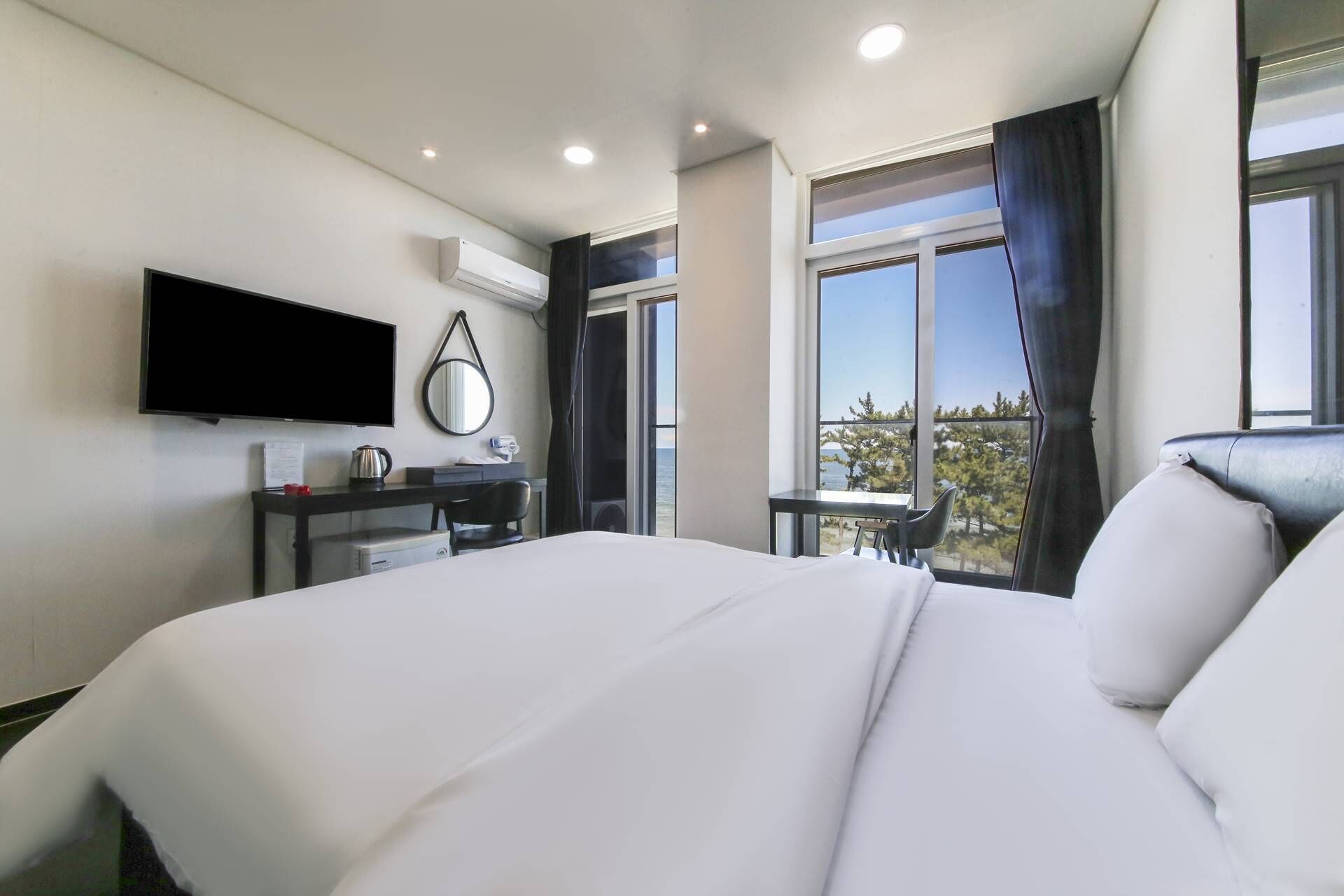 A hotel room with a bed, a desk, a flat-screen TV, a mirror, and a window with a view of the outdoors.