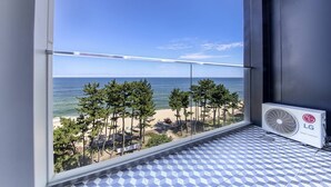 A balcony with a view of the beach and ocean, a tiled floor, and an LG Smart Inverter fan.