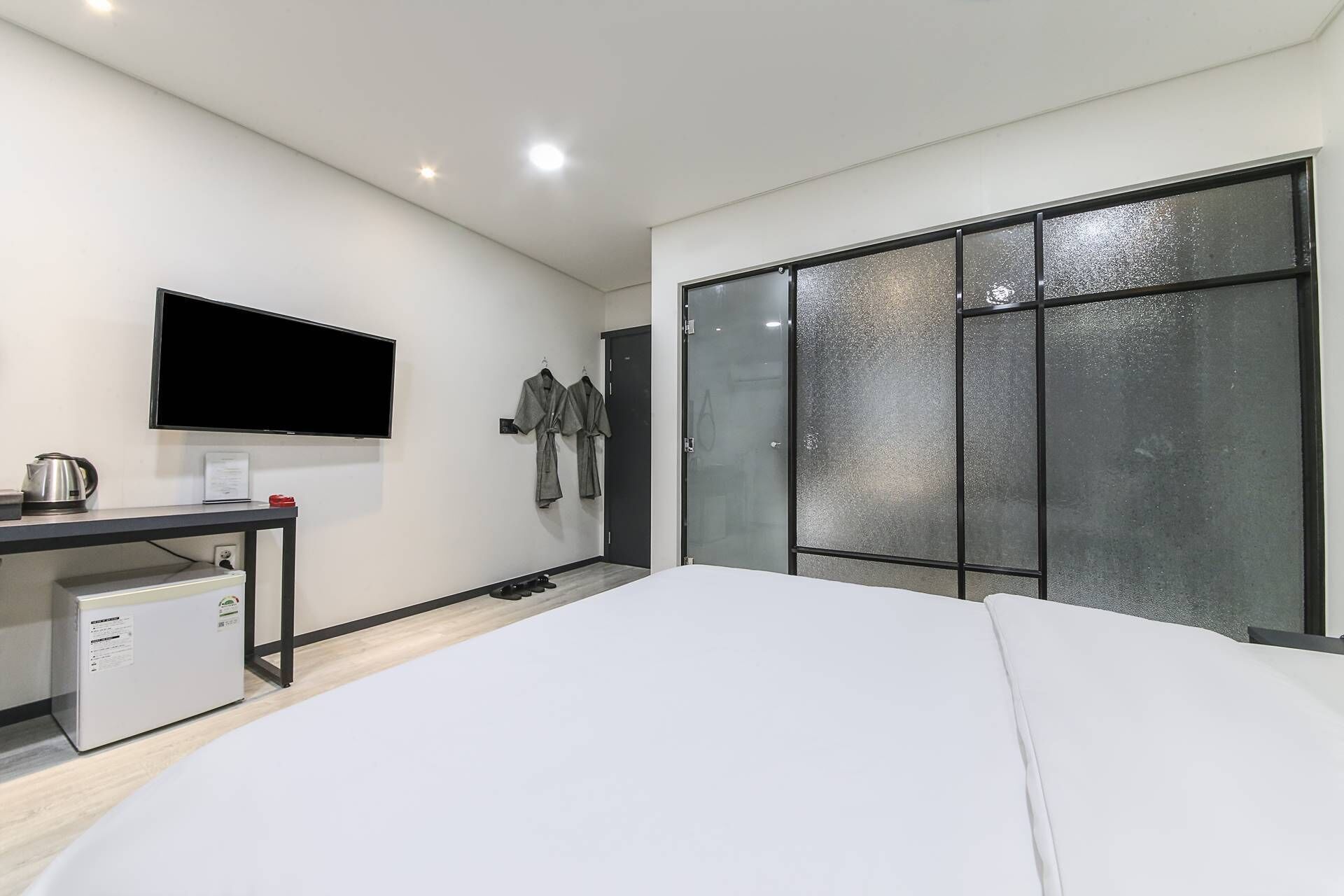 A modern hotel room with a bed, a TV, a desk with a kettle, and a wardrobe with frosted glass doors.