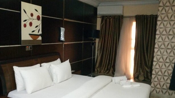 Habitació d'hotel amb un llit gran, una tauleta de nit, una obra d'art penjada a la paret i una finestra amb cortines.