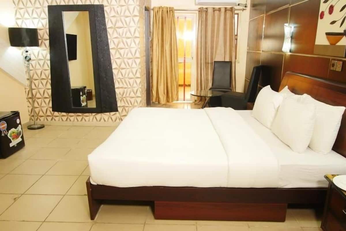 A hotel room with a large bed, a mirror, a desk, and a chair.