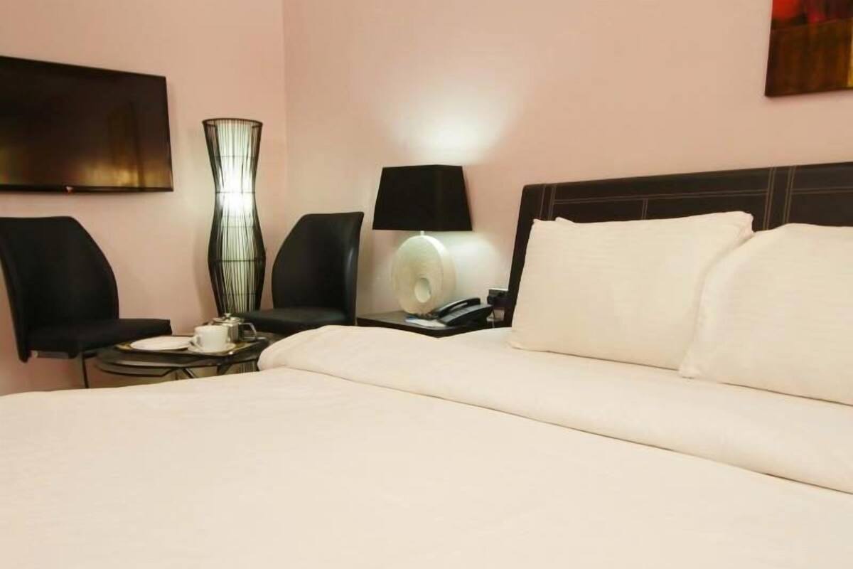 A hotel room with a bed, two chairs, a table with a lamp, and a TV mounted on the wall.