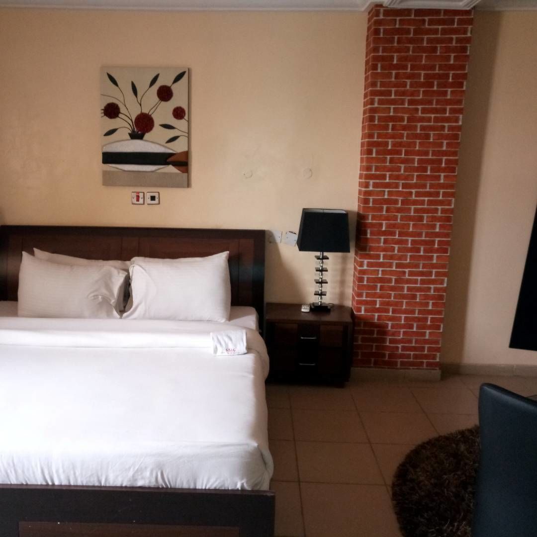 Una habitación de hotel con una cama, una mesita de noche con lámpara, una pared de ladrillo decorativa y un cuadro en la pared.