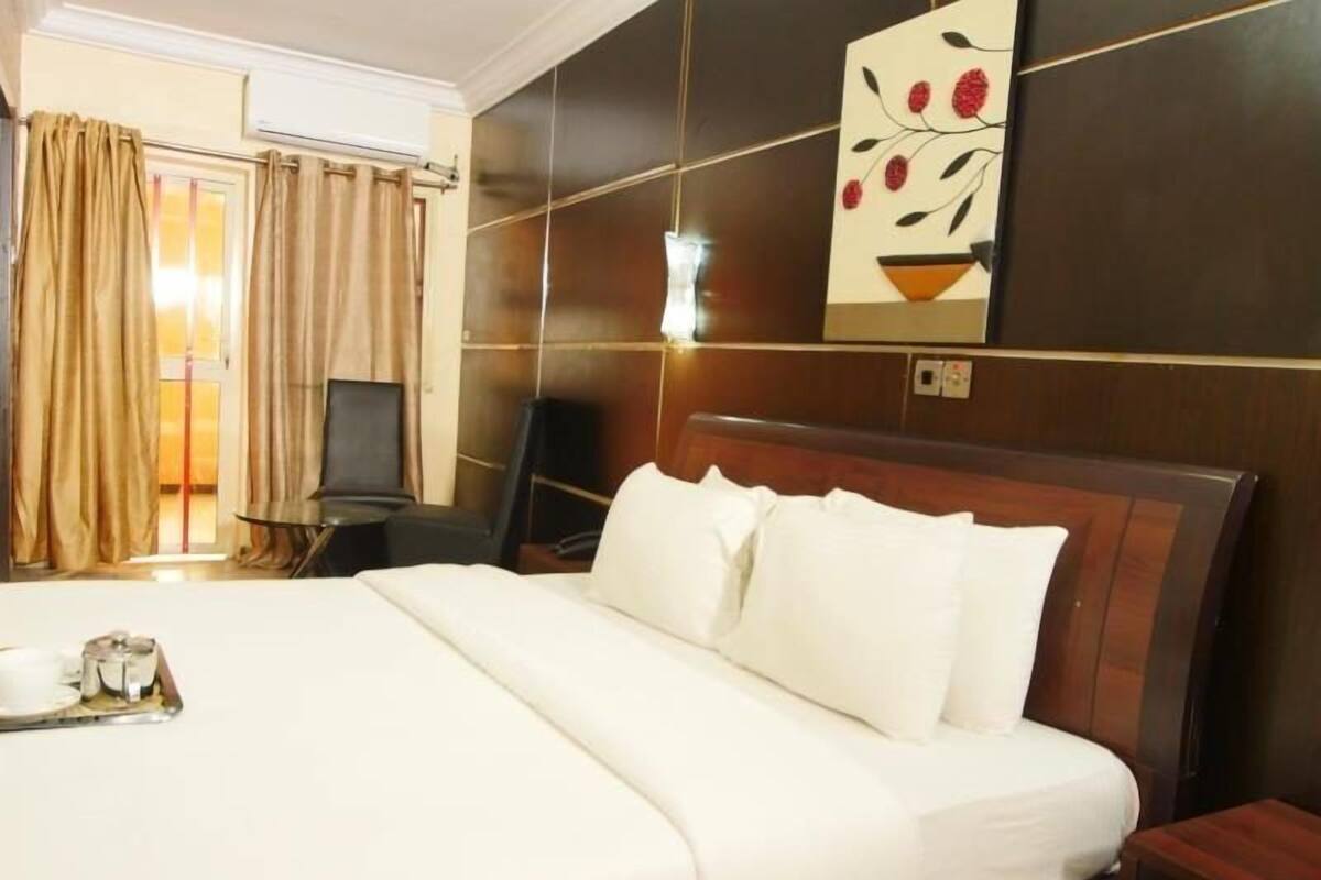 A hotel room with a large bed, a desk with a chair, a TV, and a wall-mounted artwork.