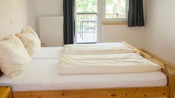 Ein Einzelbett mit Holzrahmen, weißer Bettwäsche und Blick auf eine Terrasse durch ein Fenster.