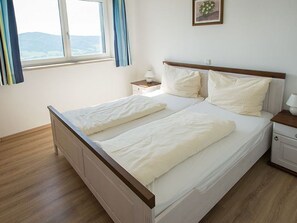 Un lit double avec une literie blanche, une tête de lit en bois, une table de chevet avec une lampe et une fenêtre avec des rideaux.