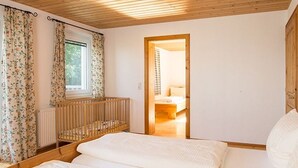 A bedroom with two beds, a wooden ceiling, a window with curtains, and a door leading to another room. - Large apartment with lake view - family holiday Stabauer (4 flowers) (Lindau)